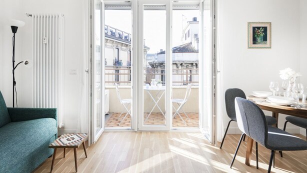 A modern living room with a sofa, a dining table set for two, and a view of the city through large glass doors.