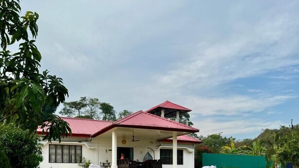 Una casa de dos pisos con techo rojo, un porche cubierto y un jardín con parterres de flores.