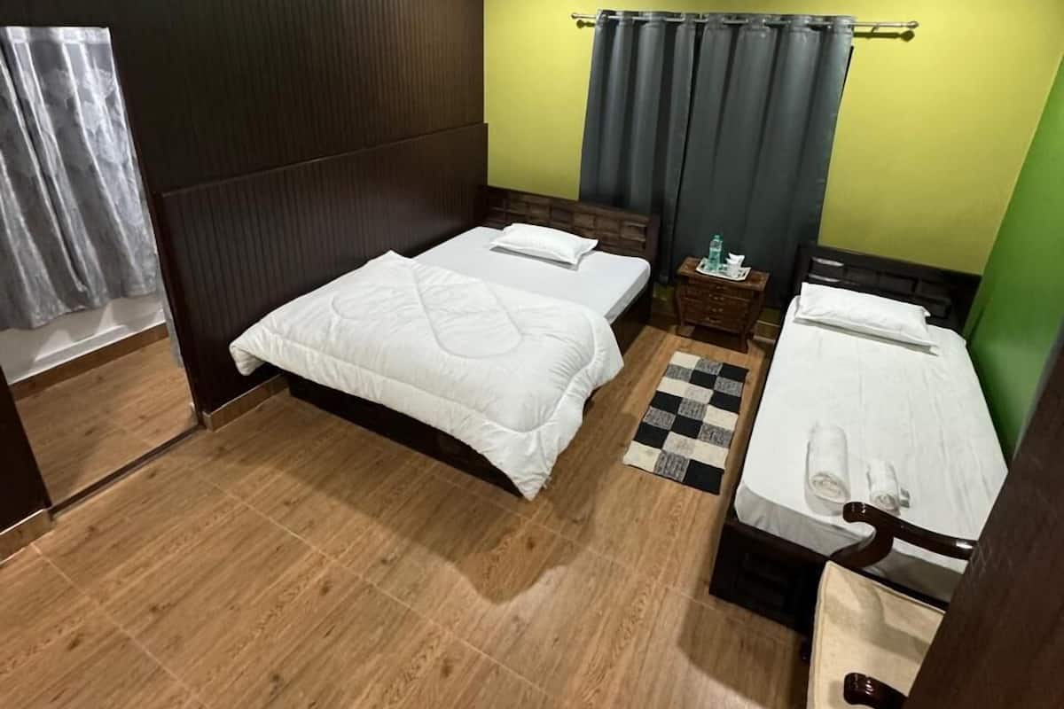 Une chambre d’hôtel avec deux lits, une petite table, une chaise, une fenêtre avec des rideaux et un ventilateur de plafond.