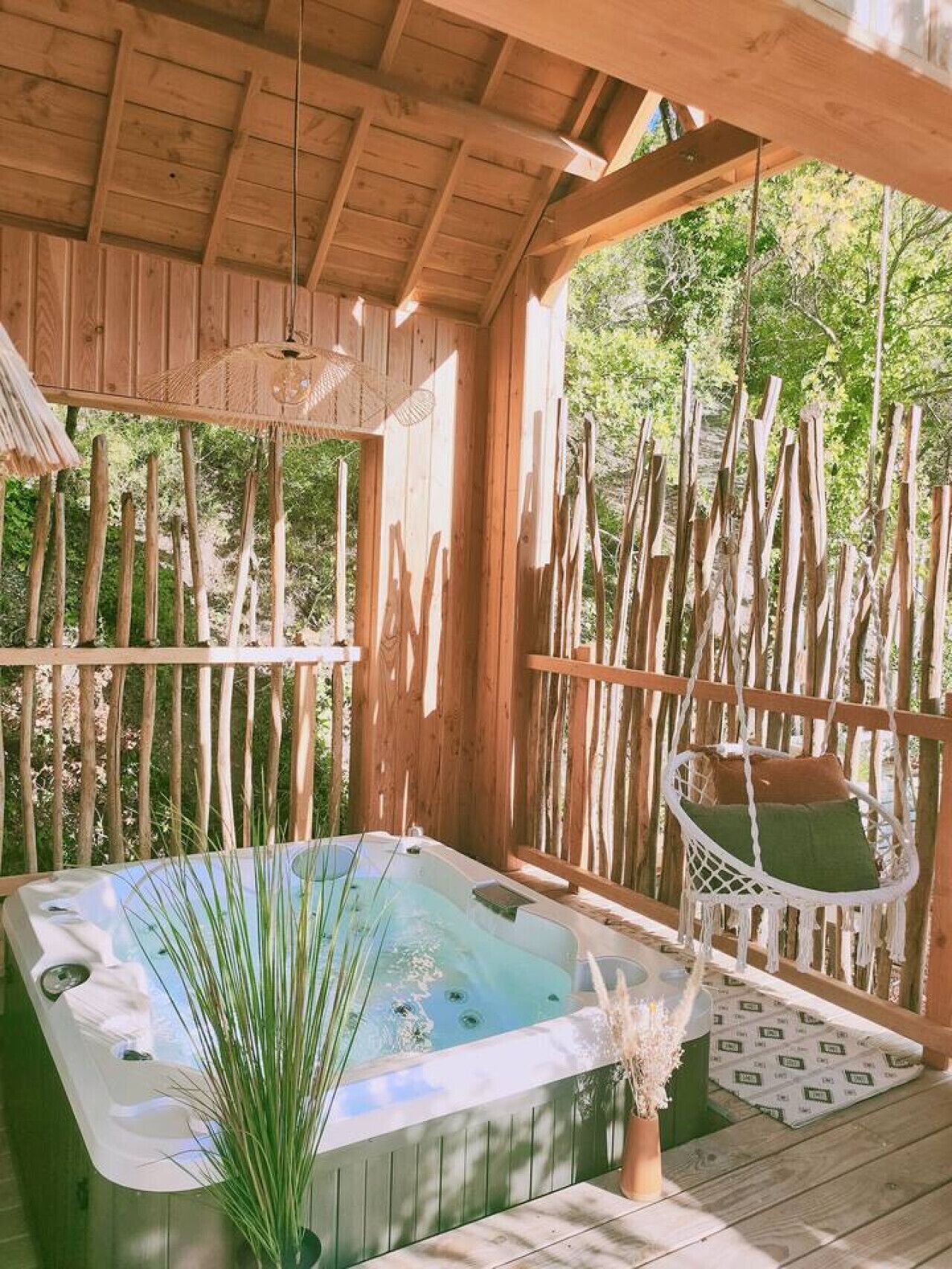 Een houten terras met een jacuzzi, een hangstoel en een potplant.