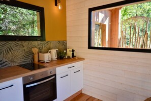 Une cuisine compacte dotée d’un plan de travail en bois, de meubles blancs, d’un four encastré et d’une fenêtre donnant sur des arbres.