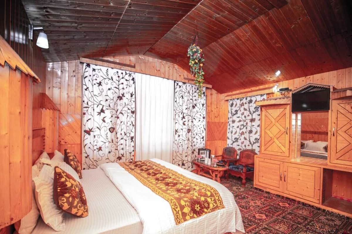 A wooden cabin bedroom with a bed, curtains, a TV, and a cabinet.