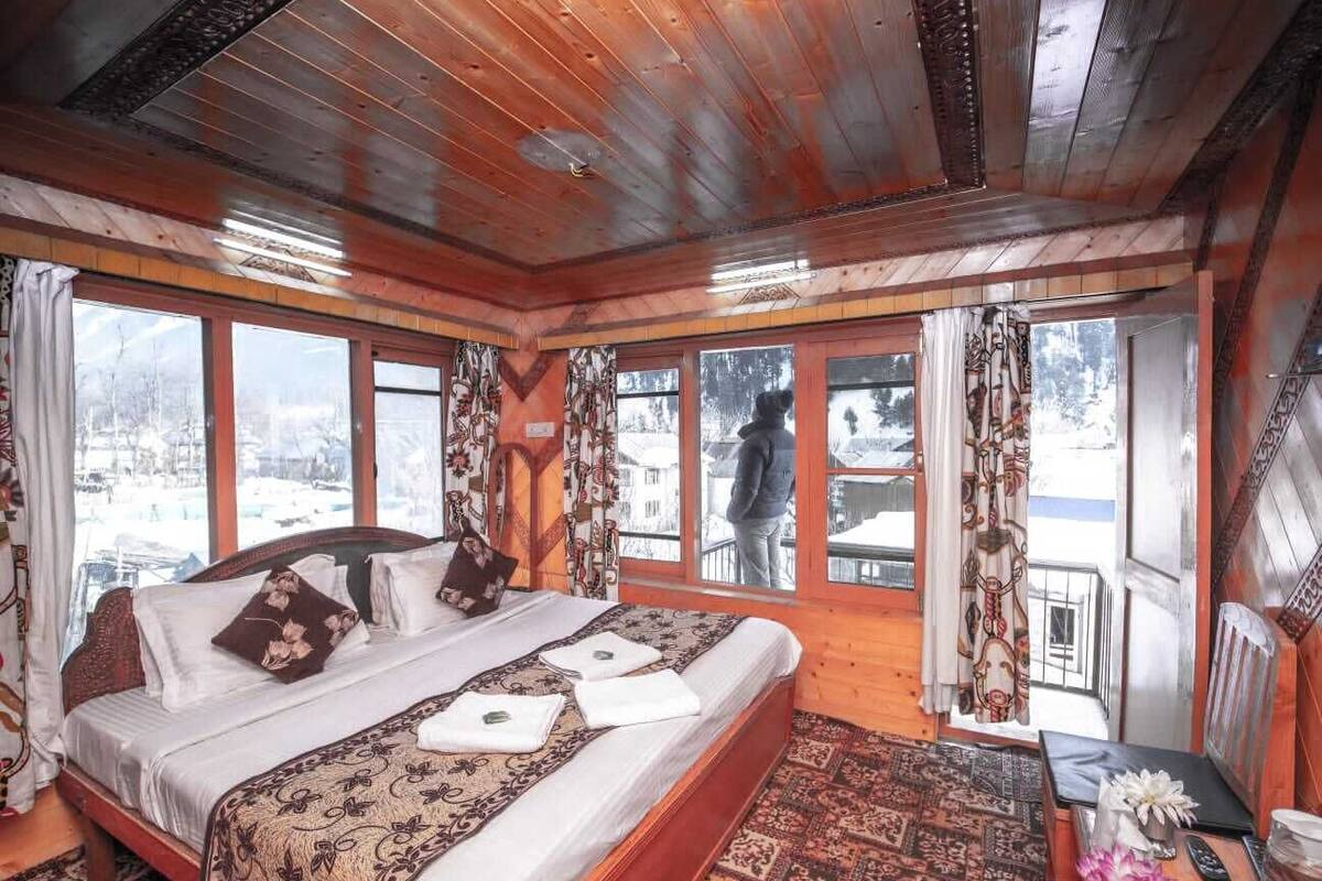 A wooden cabin bedroom with a large bed, multiple windows, and a view of a snowy landscape.