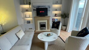 Un salon moderne comprenant un canapé, un fauteuil, une table basse, une cheminée, un téléviseur et des objets de décoration.