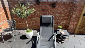 Un fauteuil de relaxation, une petite table avec une plante et un arbre en pot, le tout installé dans un espace patio agrémenté d’un mur en briques.