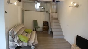 Una habitación con sofá, sillón, televisión y escalera.