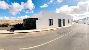 A modern white building with a flat roof, a stone wall, and a paved road in front. - Apartment Alegria in the Stunning Village of Mozaga, Lanzarote (Teguise)