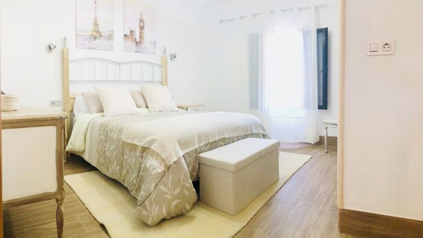 Un dormitorio con cama, mesitas de noche, un banco y obras de arte en la pared.