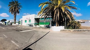A street view with a white building labeled 'BAZARROTT' and palm trees. - Apartment Alegria in the Stunning Village of Mozaga, Lanzarote (Teguise)
