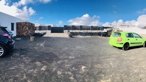 Un área de estacionamiento con un muro de piedra, un espacio de descanso techado y un edificio de fachada blanca.