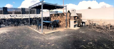 An outdoor patio with a covered seating area, stone walls, and a stone fireplace.
