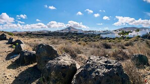 Un paisaje costero con edificios blancos, terreno rocoso y una montaña al fondo.