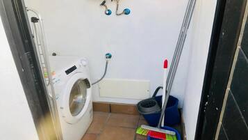 A compact laundry room with a washing machine, a small bathtub, and a mop.