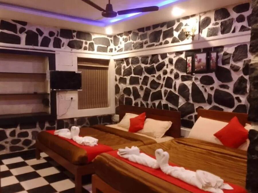 Quarto com duas camas, televisão, piso xadrez e paredes de pedra.