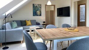 Ein modernes Wohnzimmer mit einer Loft-Decke, einem Holzesstisch, grauen Sofas und einem an der Wand befestigten Fernseher.