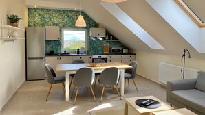 Eine moderne Küche mit Essbereich, ein Schlafzimmer im Zwischengeschoss mit Dachfenster und ein Wohnzimmer mit einer Couch.