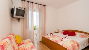 A bedroom with a bed, a sofa, a television mounted on the wall, and a window with curtains.