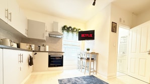 A modern kitchen with a built-in oven, a dining area with a table and chairs, a TV mounted on the wall, and a door leading to another room. - 25min to Central - Zone 2 - Free Parking - Sleep 6 (London)