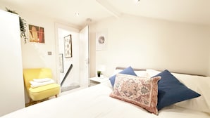 A bedroom with a bed, a bedside table, a chair, and a door leading to another room. - 25min to Central - Zone 2 - Free Parking - Sleep 6 (London)