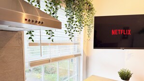 A modern kitchen with a stainless steel range hood, a window with blinds, a television mounted on the wall, and a small table with a plant. - 25min to Central - Zone 2 - Free Parking - Sleep 6 (London)