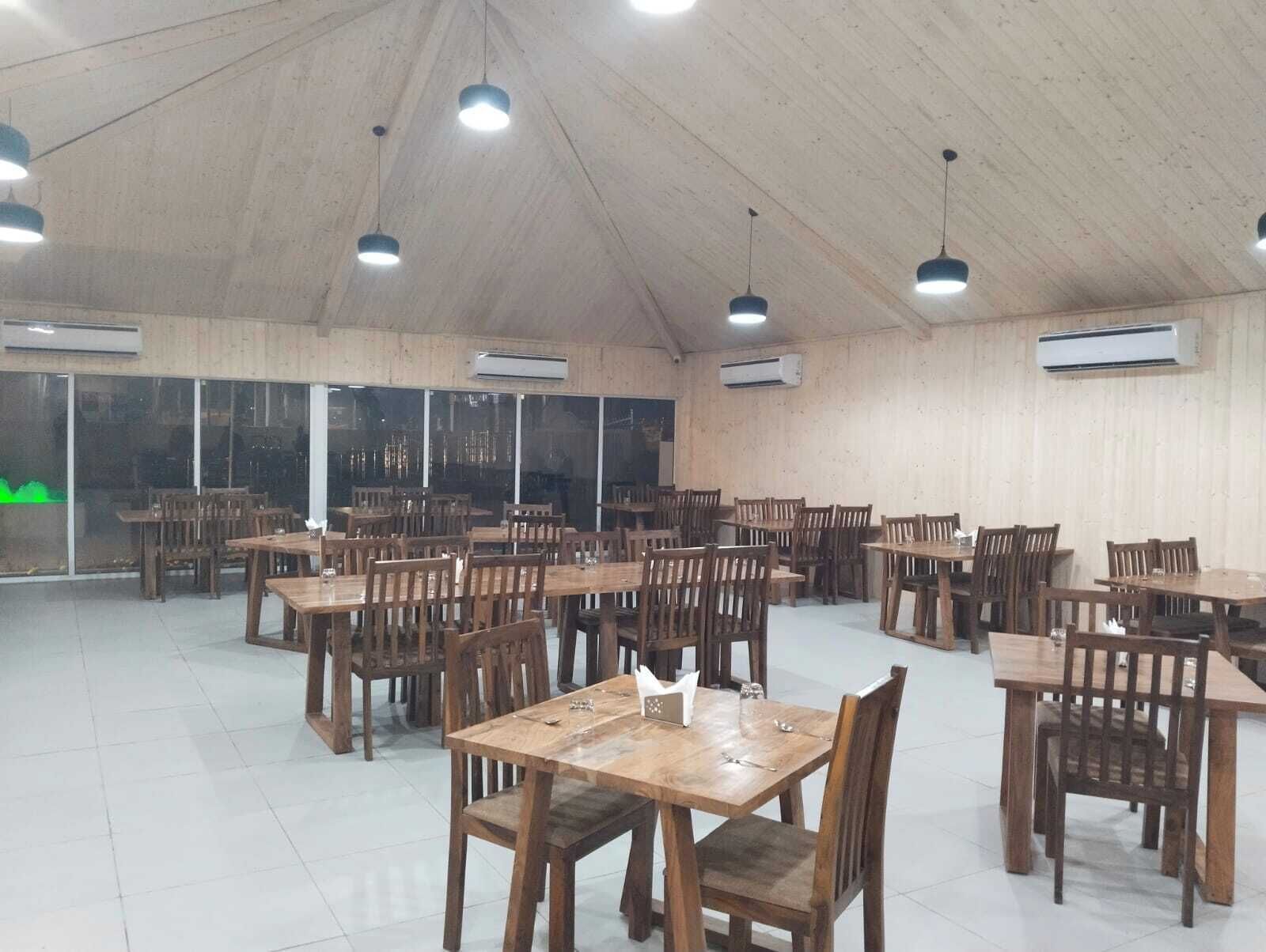 A spacious dining area with wooden tables and chairs, large windows, and ceiling lights.