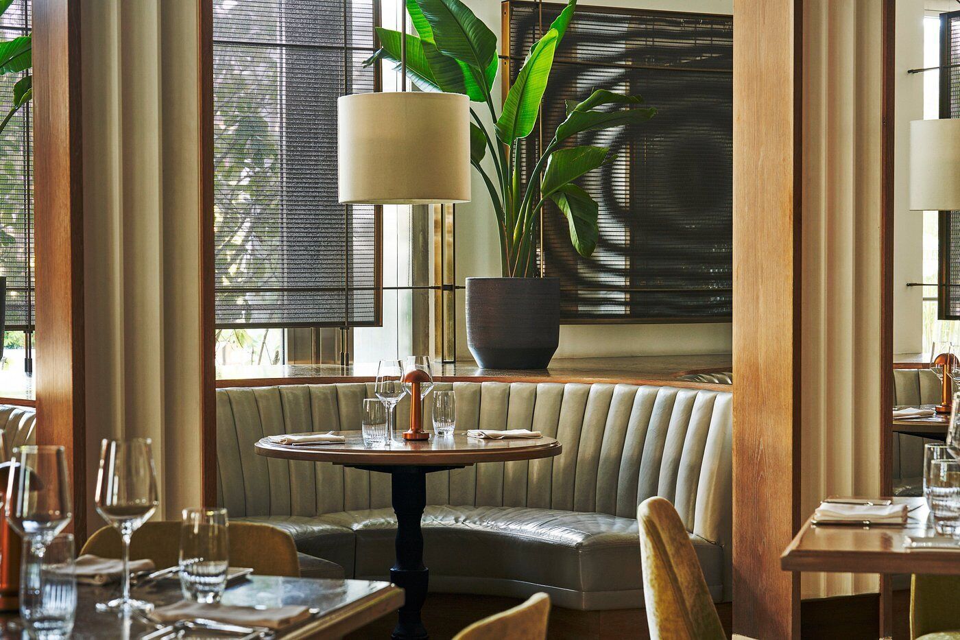 A restaurant interior with a round table, cushioned bench, and a potted plant.