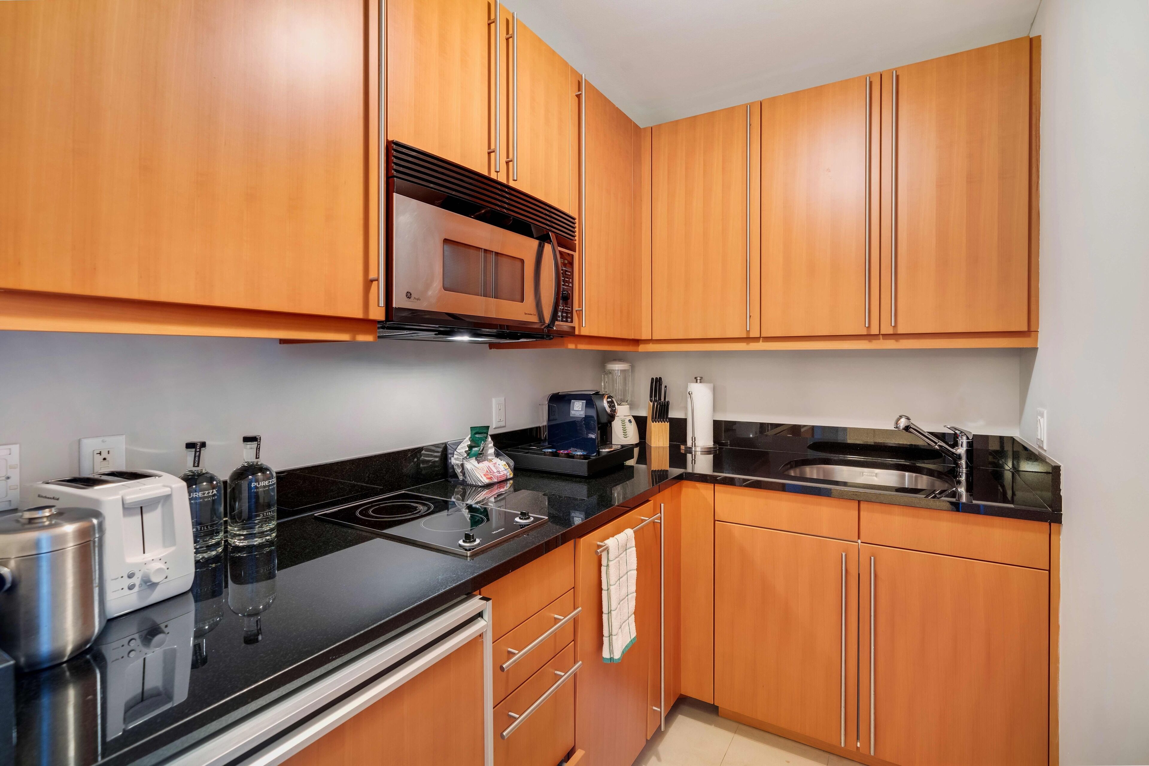 A modern kitchen with wooden cabinets, a black countertop, a microwave, a toaster, and a sink.