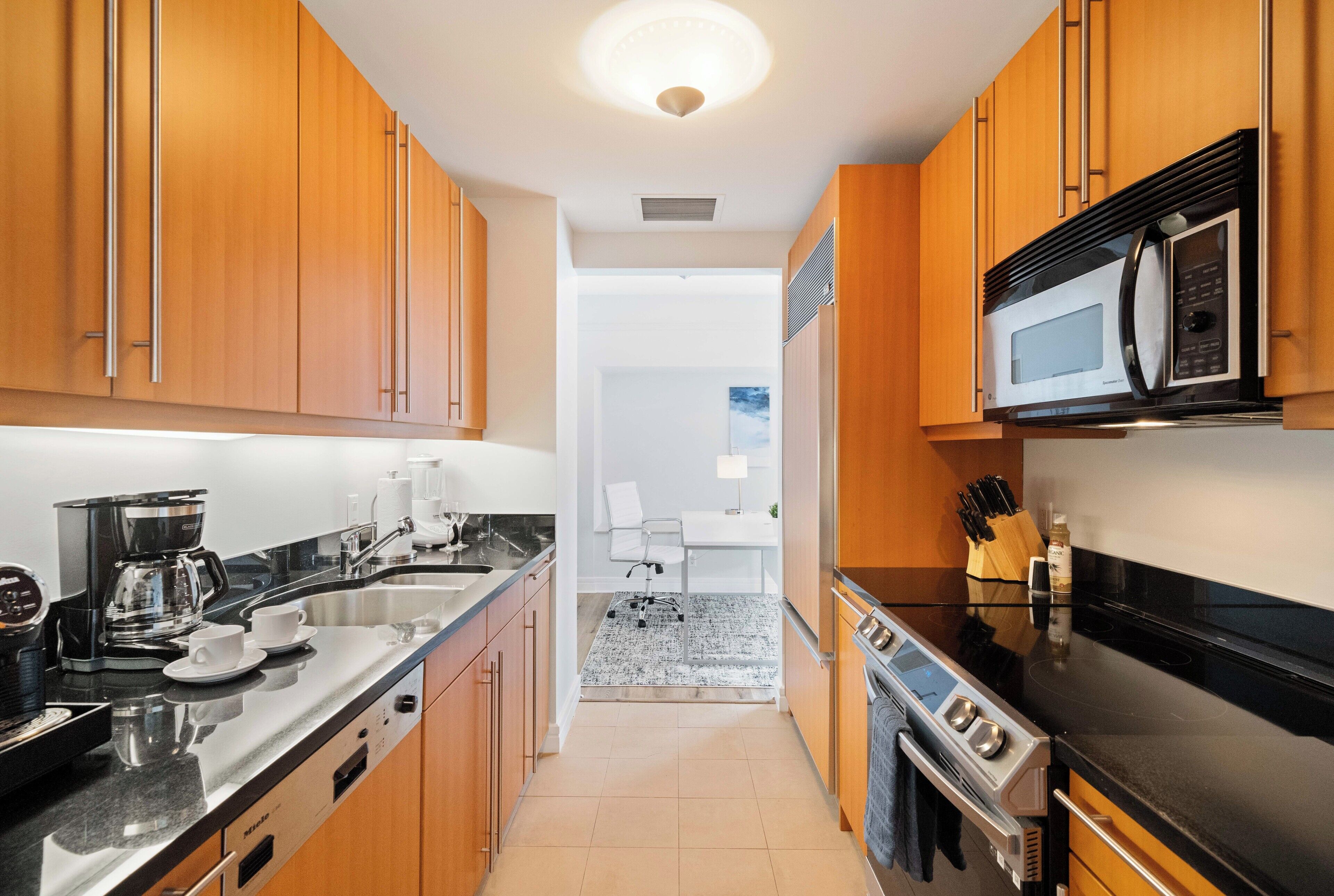 A modern kitchen with wooden cabinets, a stainless steel countertop, a built-in microwave, and a coffee maker.