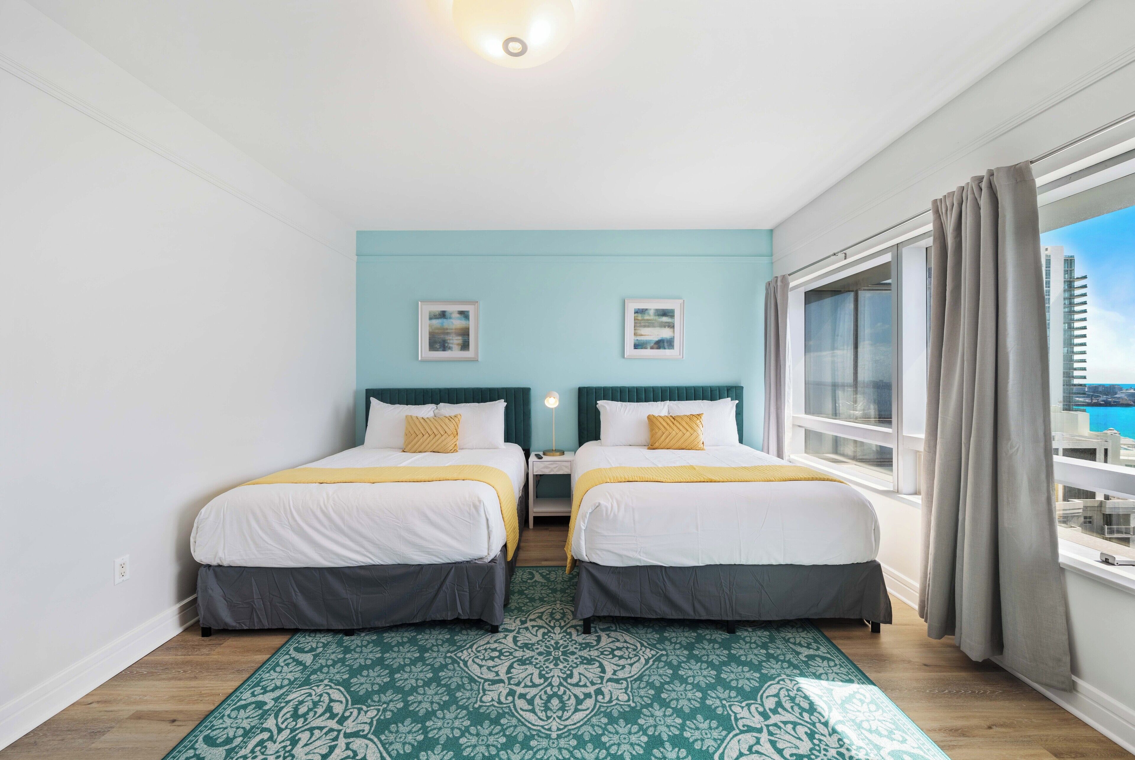 Une chambre double avec deux lits, un mur d’accent de couleur turquoise, une vue sur la ville et un tapis à motifs.