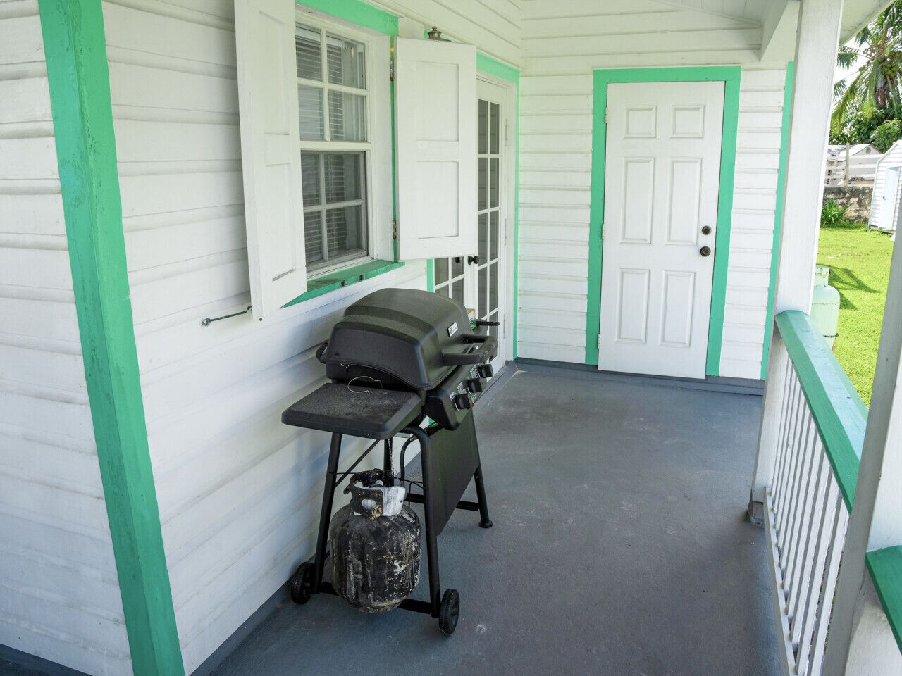 A covered porch with a grill and propane tank.