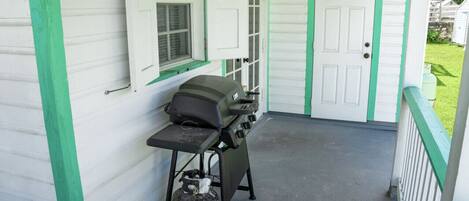 A covered porch with a grill and propane tank.