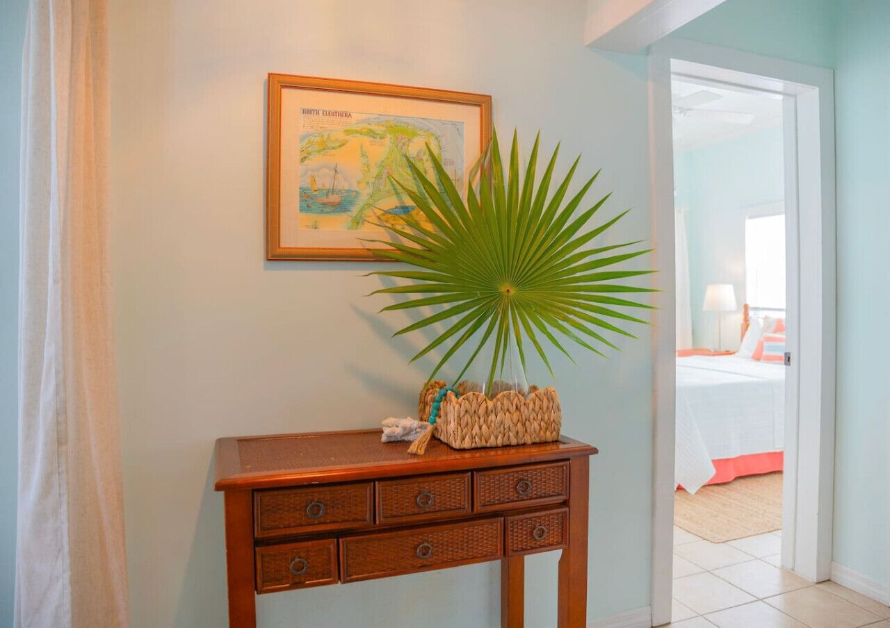 A wooden console table with drawers, a framed map on the wall, and a large potted plant.