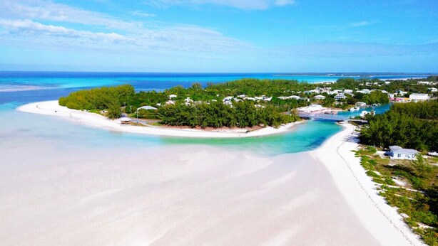 An aerial view of a beach with clear turquoise waters, a white sandy shore, and a small island with dense greenery and buildings. - Swim. Fish. Sun. Repeat. | Spanish Wells Oceanfront Escape (Spanish Wells)
