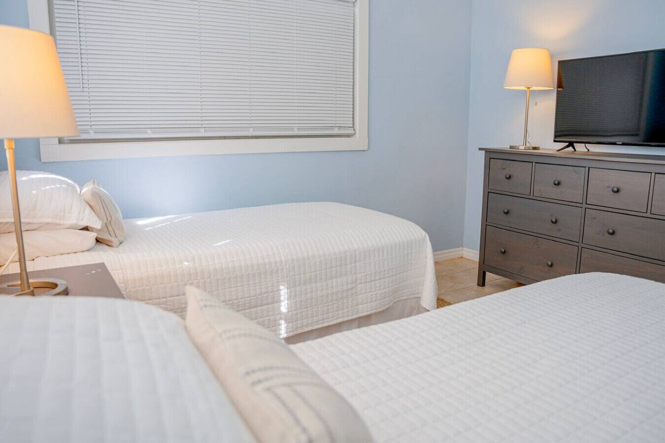 Une chambre d’hôtel avec deux lits, une commode, un téléviseur et deux lampes.