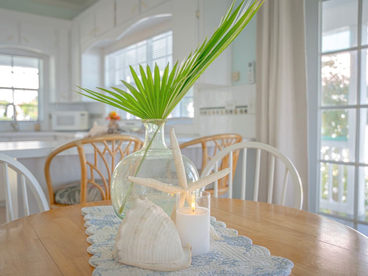 A dining table with a glass vase containing a green plant and a starfish, a candle, and a seashell.