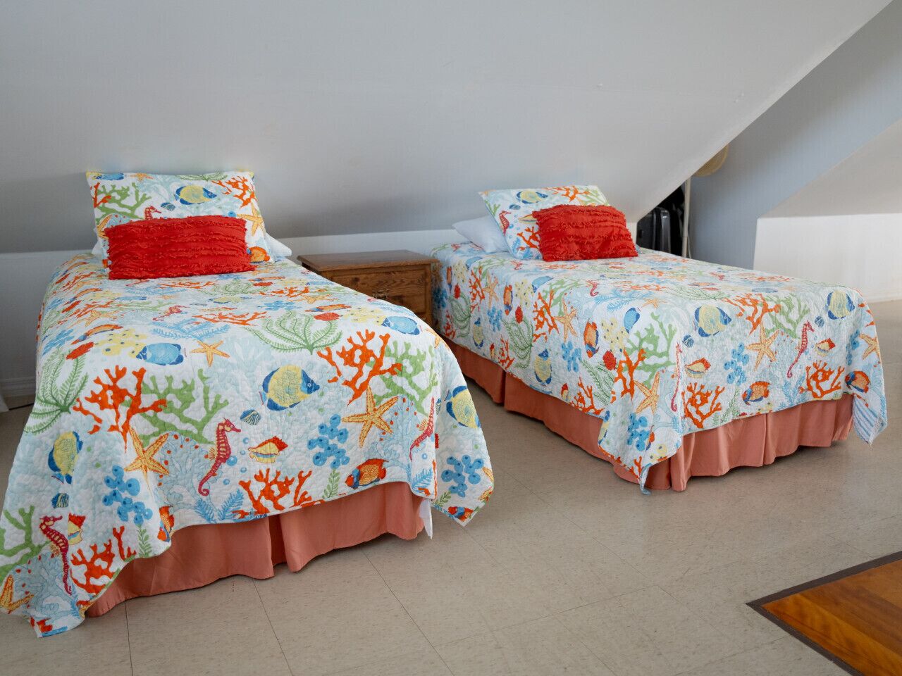 Une chambre avec deux lits, chacun agrémenté d’une couvre-lit aux couleurs vives sur le thème des récifs coralliens et d’un oreiller rouge.