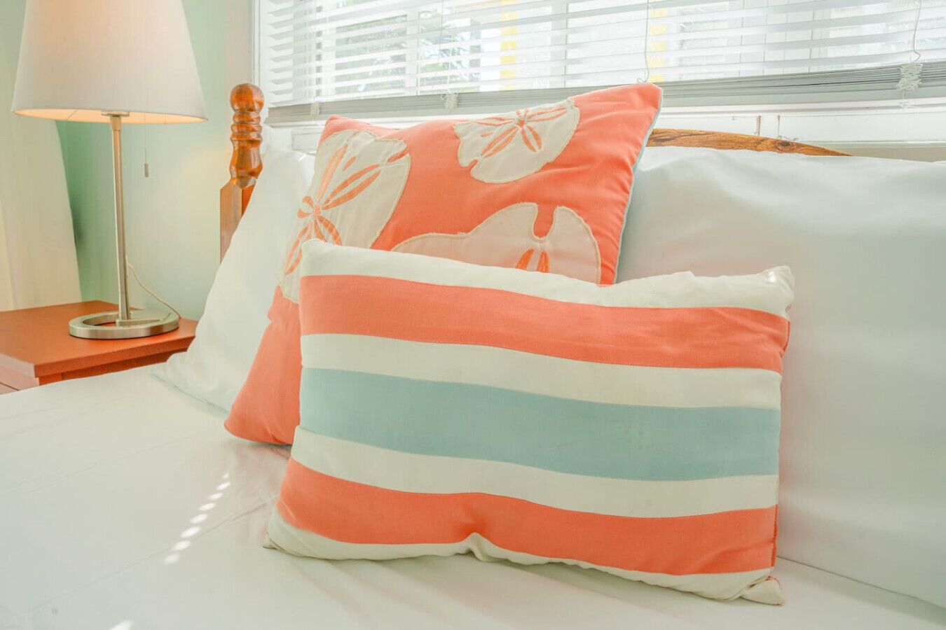 A bed with white bedding, a striped pillow, and a floral pillow.