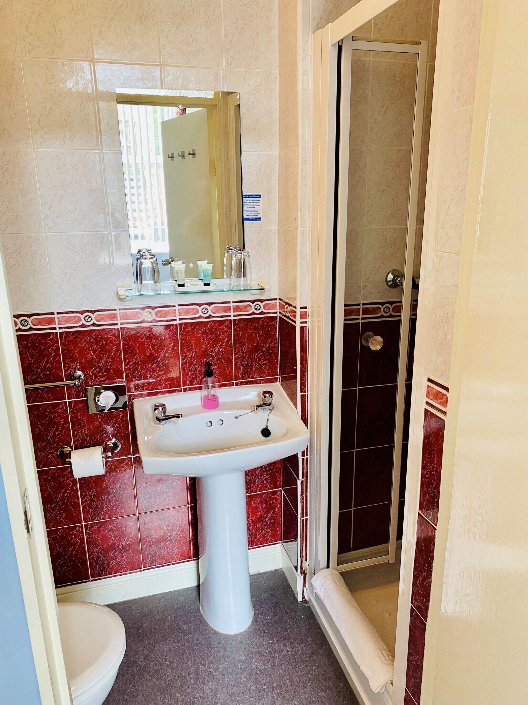 A bathroom with a white pedestal sink, red and white tiled walls, a glass shower enclosure, and a visible toilet.