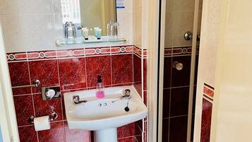A bathroom with a white pedestal sink, red and white tiled walls, a glass shower enclosure, and a visible toilet.