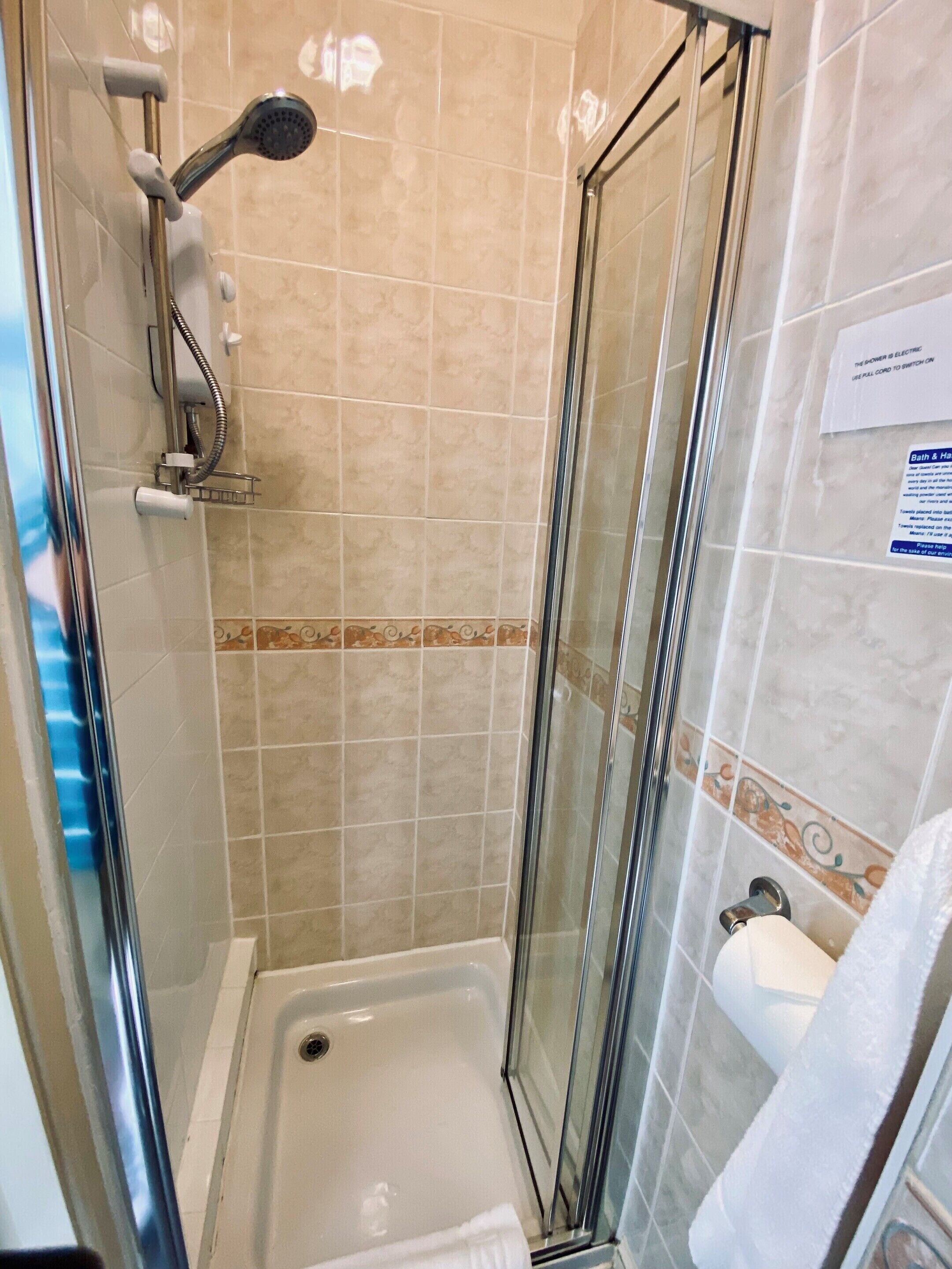 Eine Duschkabine mit Glaswänden, eine Handbrause, ein Handtuchhalter und ein Toilettenpapierhalter.