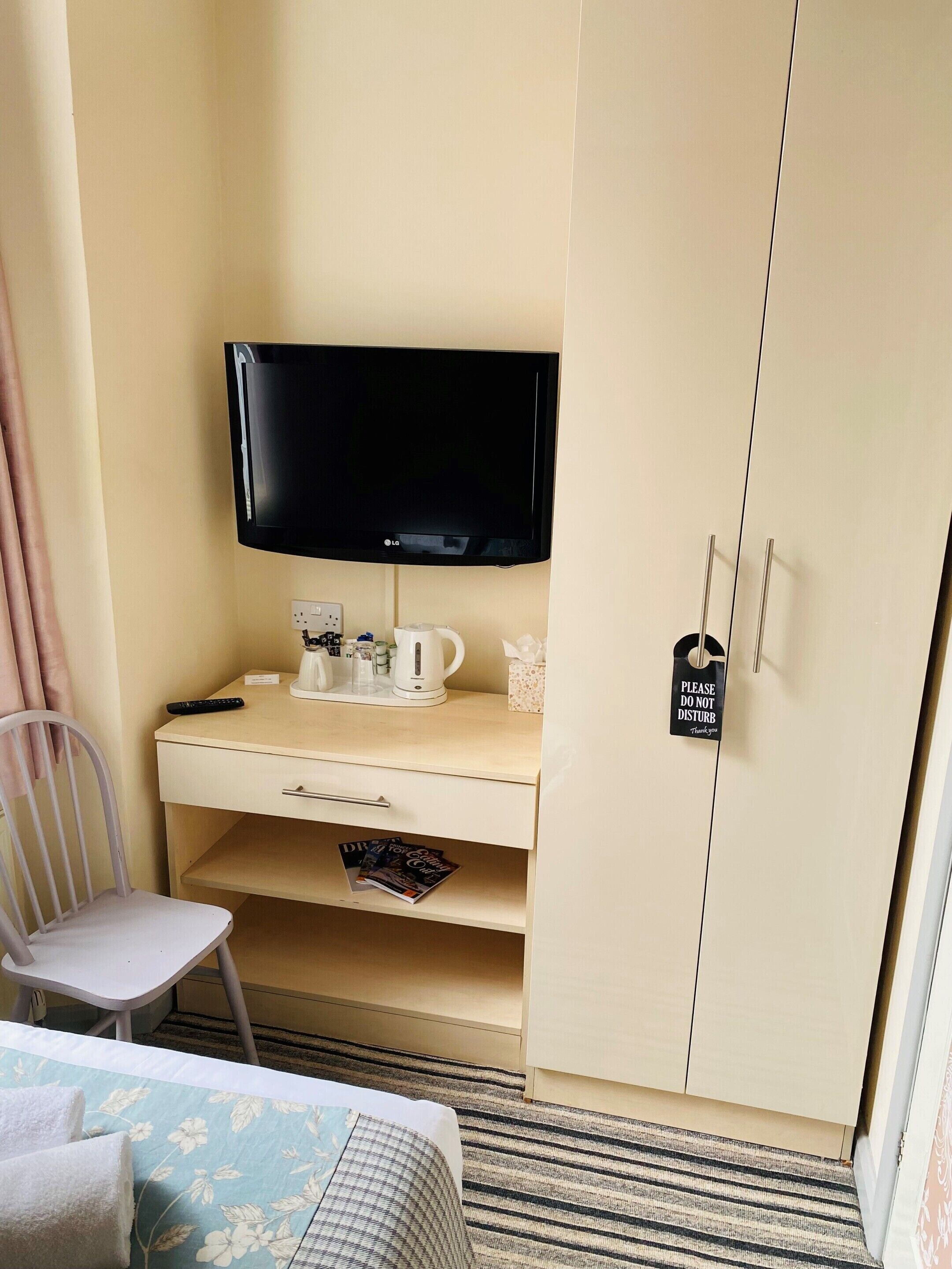 A hotel room with a bed, a desk with a television, a chair, and a wardrobe.