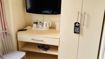 A hotel room with a bed, a desk with a television, a chair, and a wardrobe.