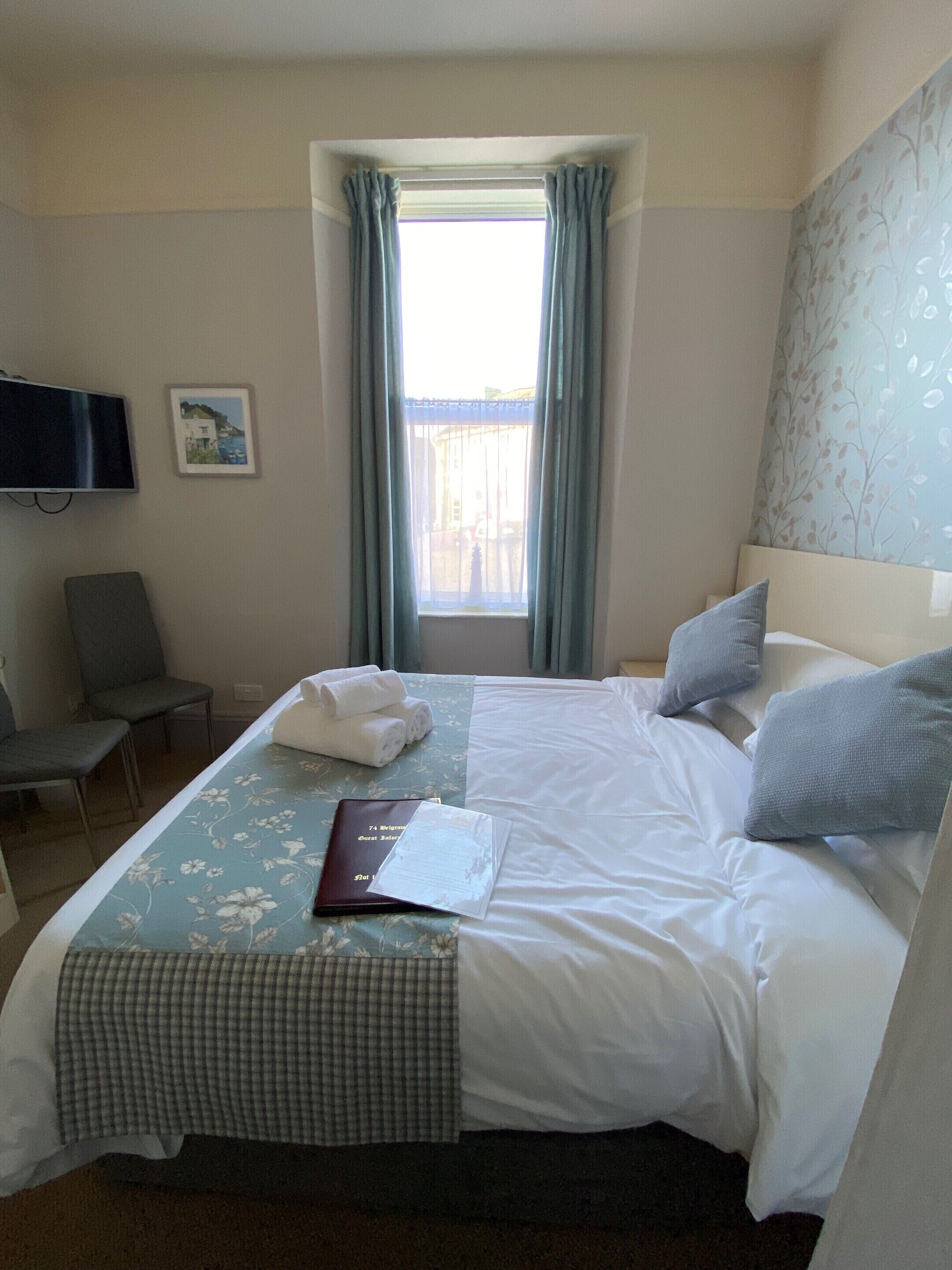 Une chambre d’hôtel avec un lit, une chaise, un bureau, une télévision et une fenêtre avec des rideaux.
