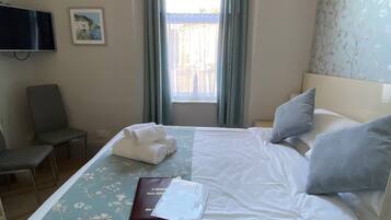 Une chambre d’hôtel avec un lit, une chaise, un bureau, une télévision et une fenêtre avec des rideaux.