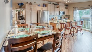 Una cocina moderna con armarios de madera, electrodomésticos de acero inoxidable y un comedor con cuatro sillas y una mesa dispuesta para cuatro comensales.