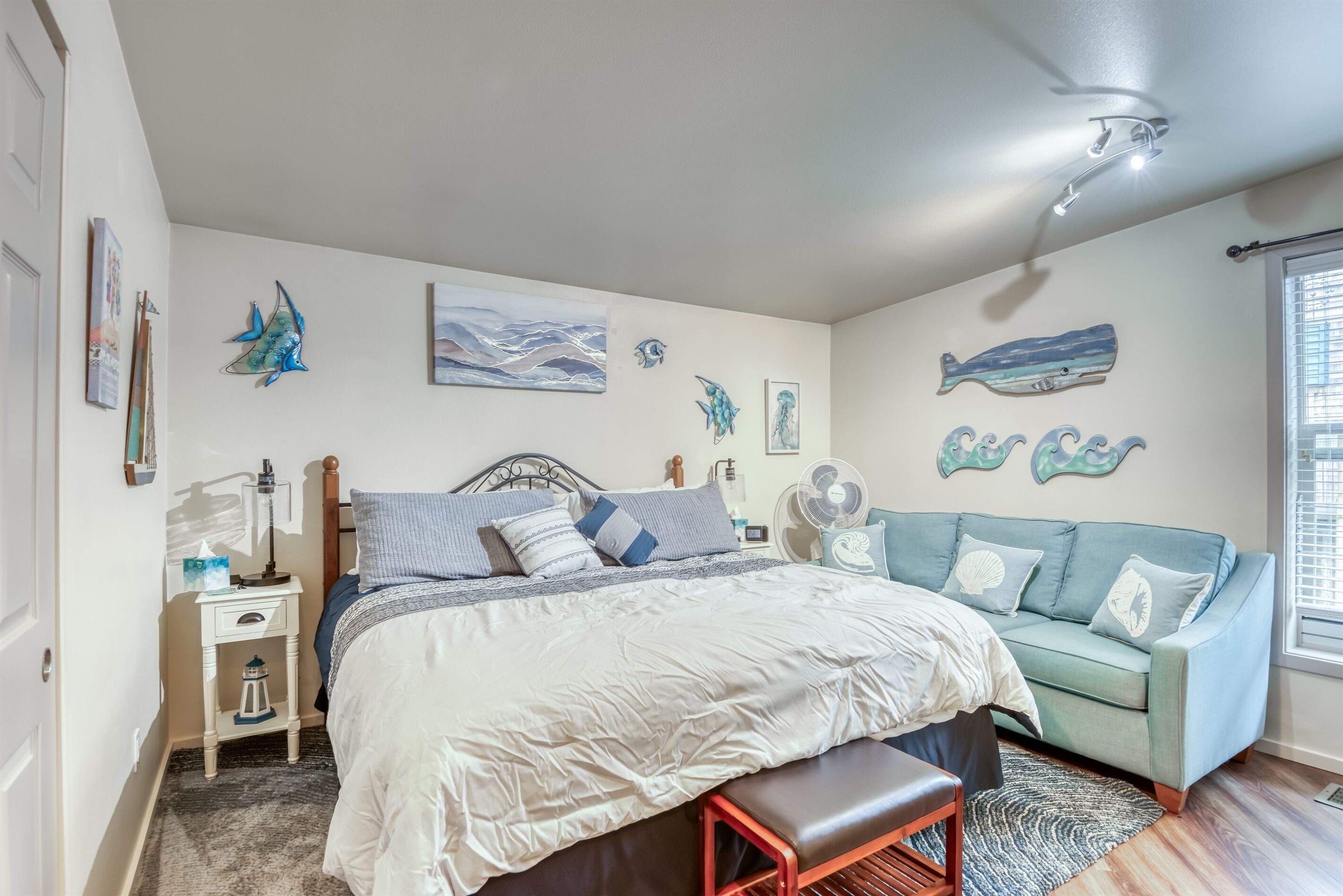 A bedroom with a bed, a nightstand, a bench, a fan, and a couch.
