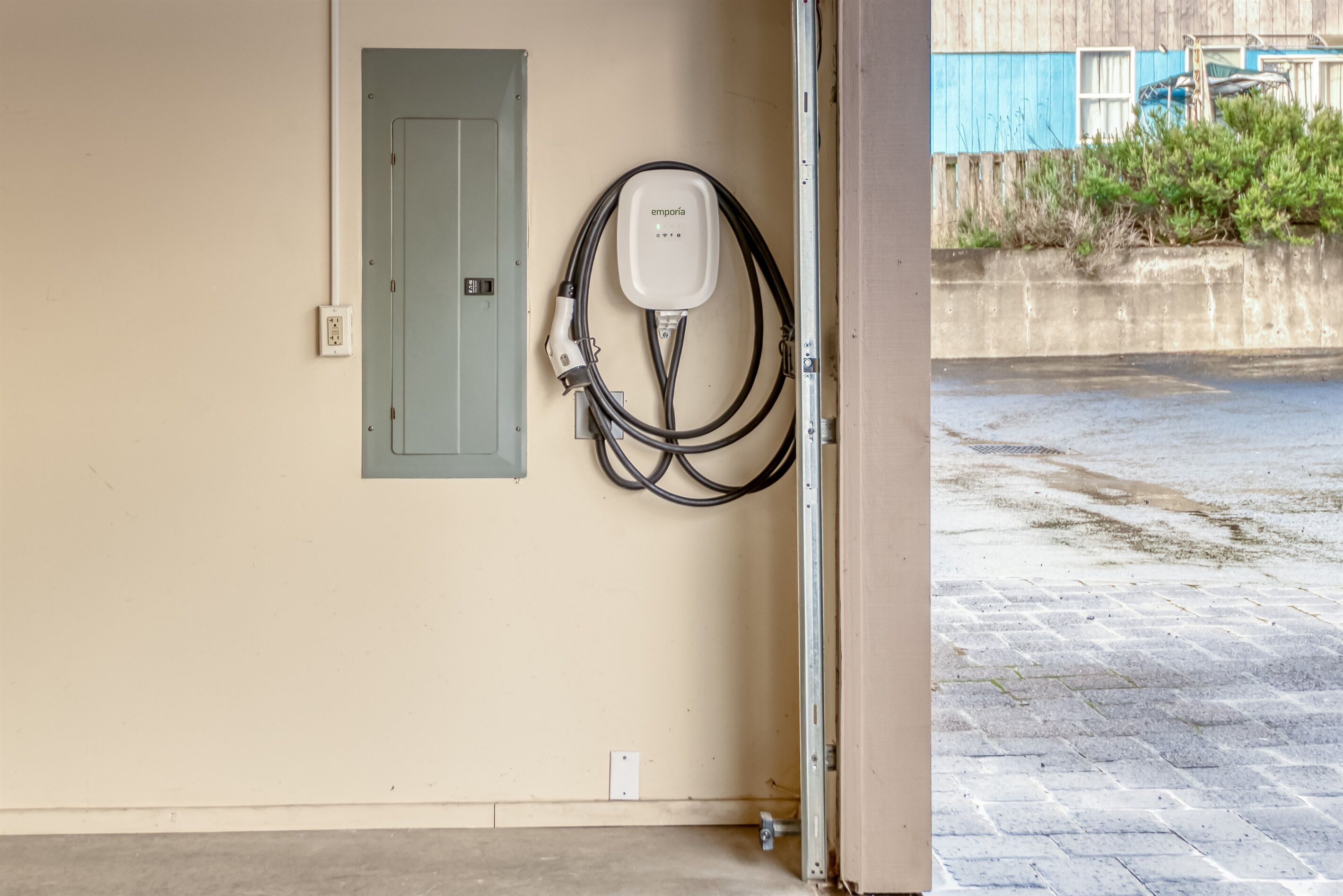 Puerta de garaje abierta con una estación de carga para vehículos eléctricos montada en la pared.