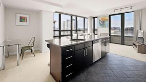 A modern kitchen with a large island, black cabinets, and a view of the city through large windows. - Easy Downtown DC Access , 2BR w/ Terrace + Gym (Arlington)