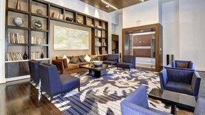 A modern living room with a large bookshelf, comfortable seating, and a patterned rug. - Easy Downtown DC Access , 2BR w/ Terrace + Gym (Arlington)