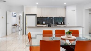 A modern kitchen with white cabinets, a stainless steel refrigerator, and a glass dining table with orange chairs. - The Canadian Escape, Ballarat - Up to 10 guests! (Canadian)